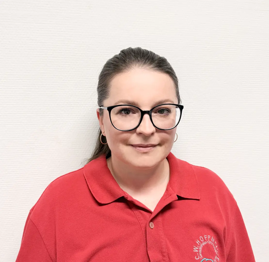 Laechelnde Frau mit Brille und rotem Poloshirt vor heller Wand
